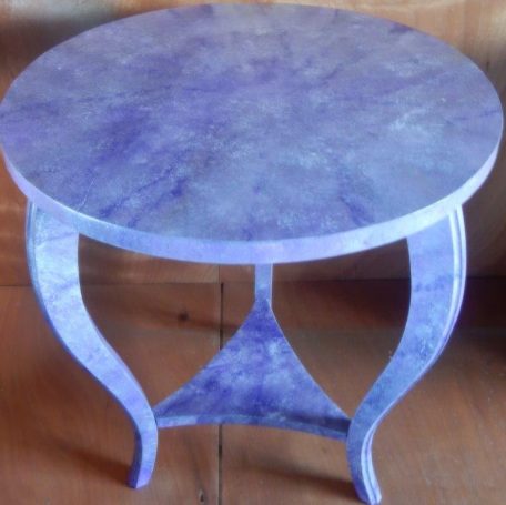 Table ronde en bois aux jambes courbées, finition violette marbrée.