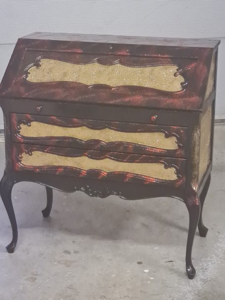 Commode vintage en bois noir et doré, avec des courbes élégantes et deux tiroirs.