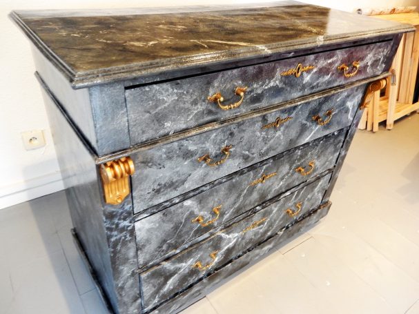 Commode en marbre gris avec quatre tiroirs et poignées dorées.