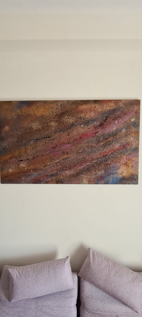 Œuvre d'art en bois aux couleurs chaudes, accrochée au mur au-dessus d'un canapé.